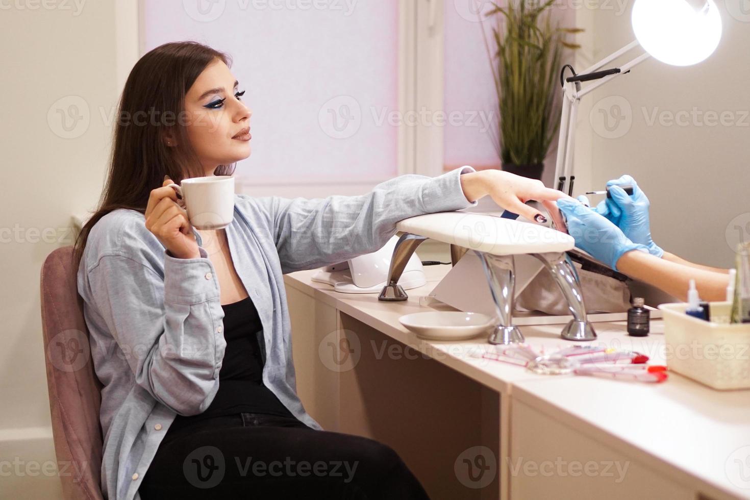 Frau bekommt Maniküre in einem Salon und hält eine weiße Tasse Kaffee foto