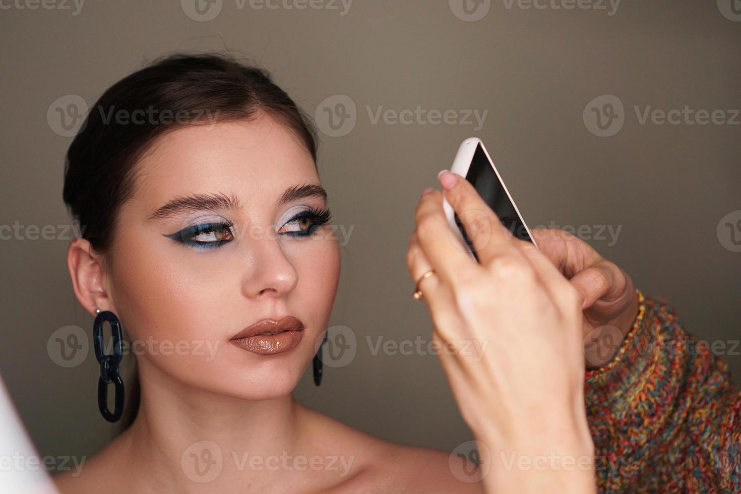 Visagistin macht Handyfoto für das Model mit Make-up foto