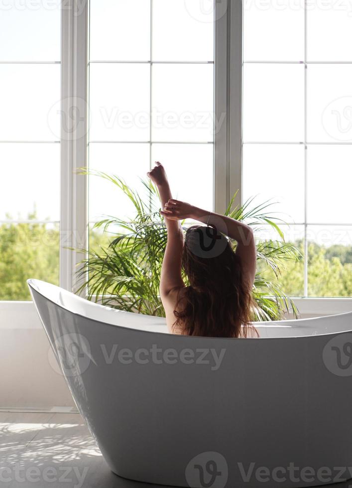 Rückseitenporträt einer fitten schlanken Frau gegen das Fenster im Badezimmer foto