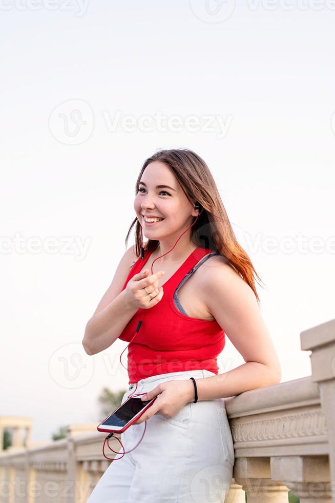 Mädchen, das im Park steht, Musik hört und plaudert foto