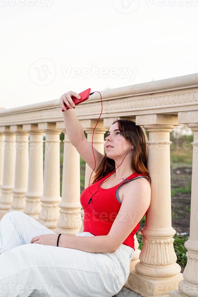 Mädchen sitzt neben der Säule, macht Selfie und hört Musik foto