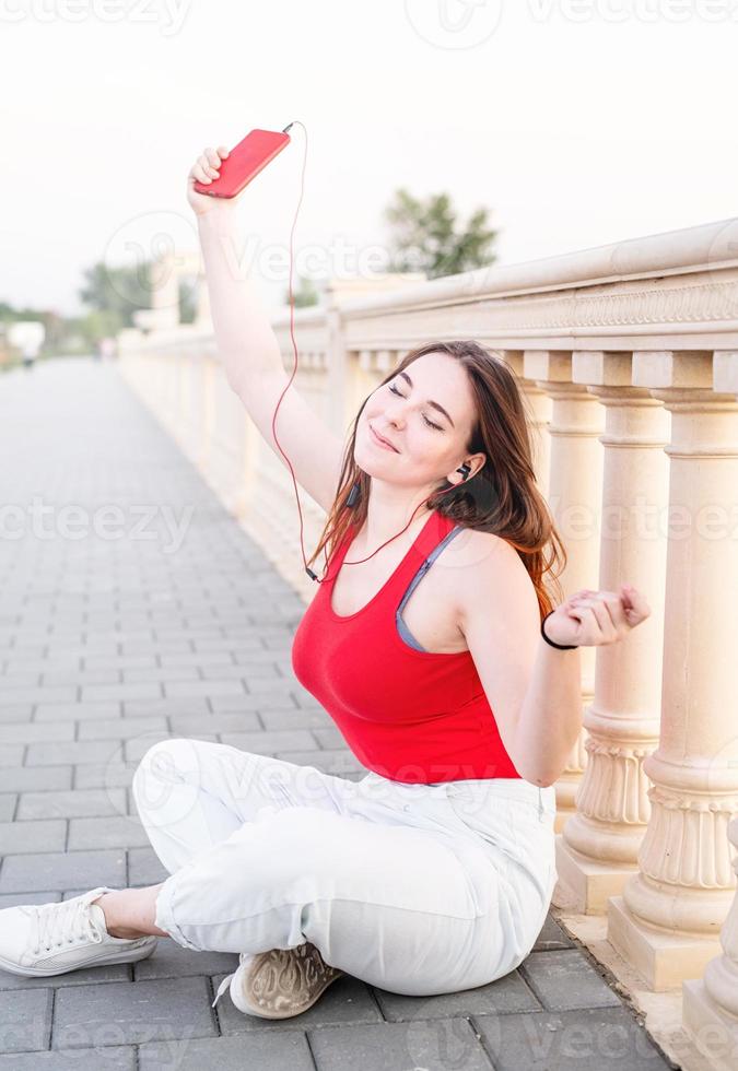 Mädchen sitzt neben dem Säulenzaun und hört Musik foto