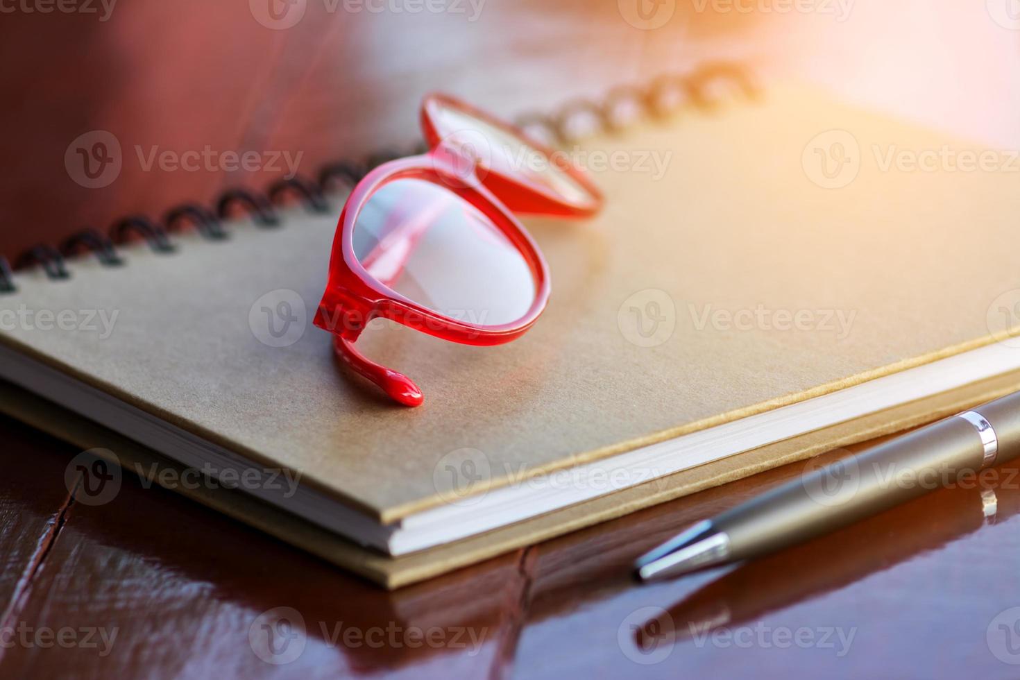 rote brille auf notizbuch mit stift- und holzhintergrund foto