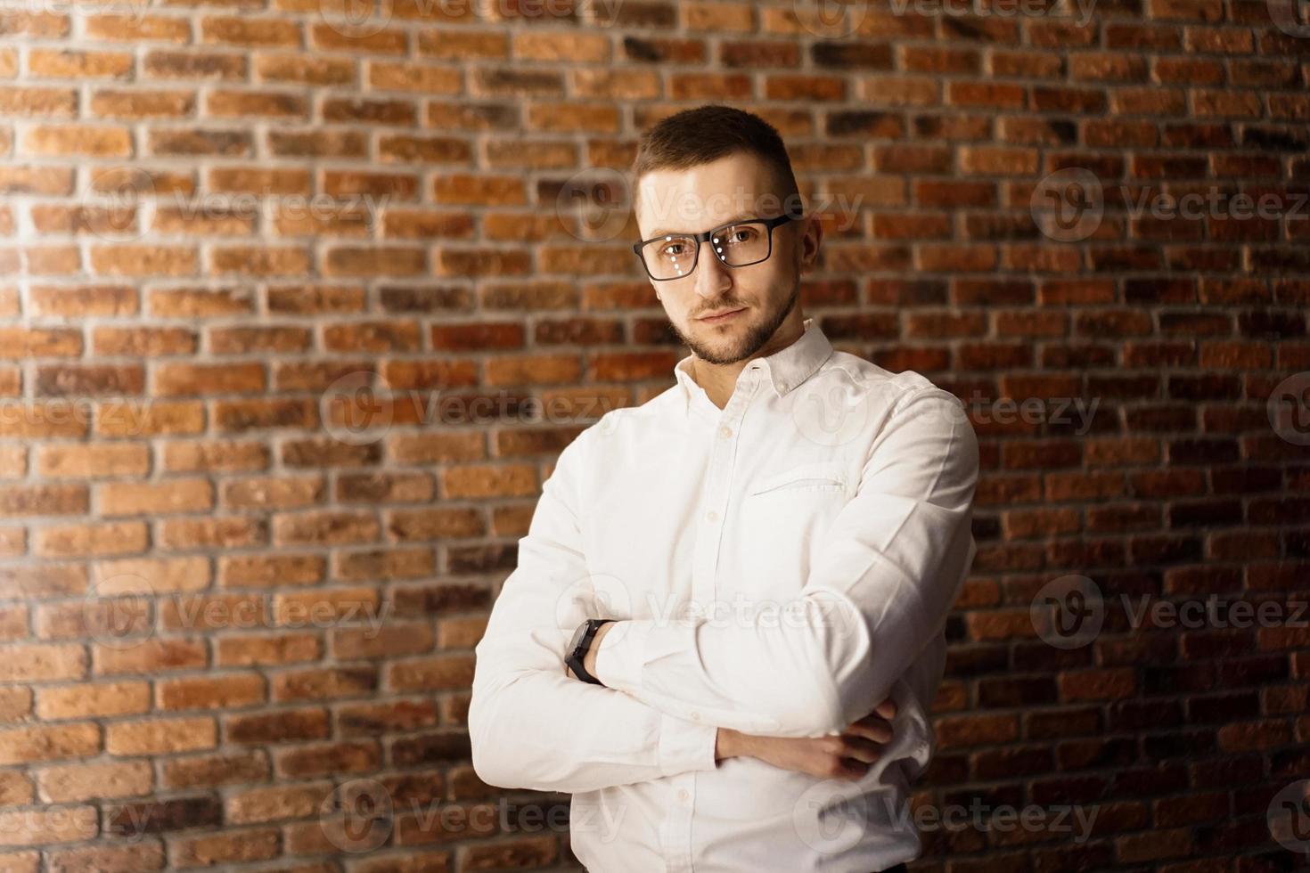 gut aussehender Mann mit Brille, der in der Nähe einer roten Backsteinmauer steht foto