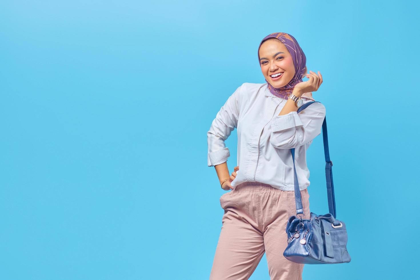 fröhliche junge Frau, die eine Tasche auf blauem Hintergrund hält foto