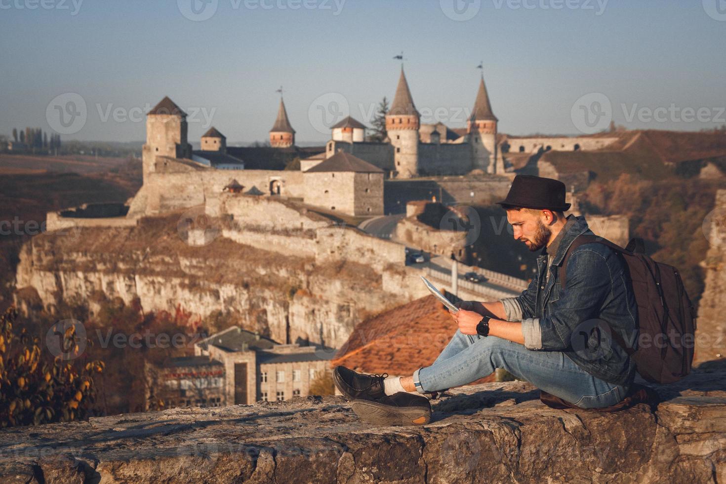 Reisender Mann mit einer Karte in den Händen sitzt auf dem Hintergrund der alten Burg foto