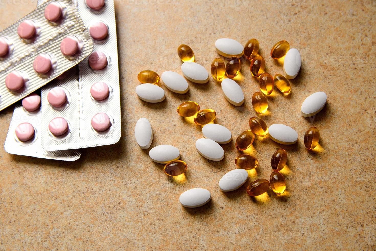 Blister mit rosa Tabletten und Vitamin D und Kapseln mit Fischöl liegen chaotisch vor dem Hintergrund einer Sandarbeitsplatte foto