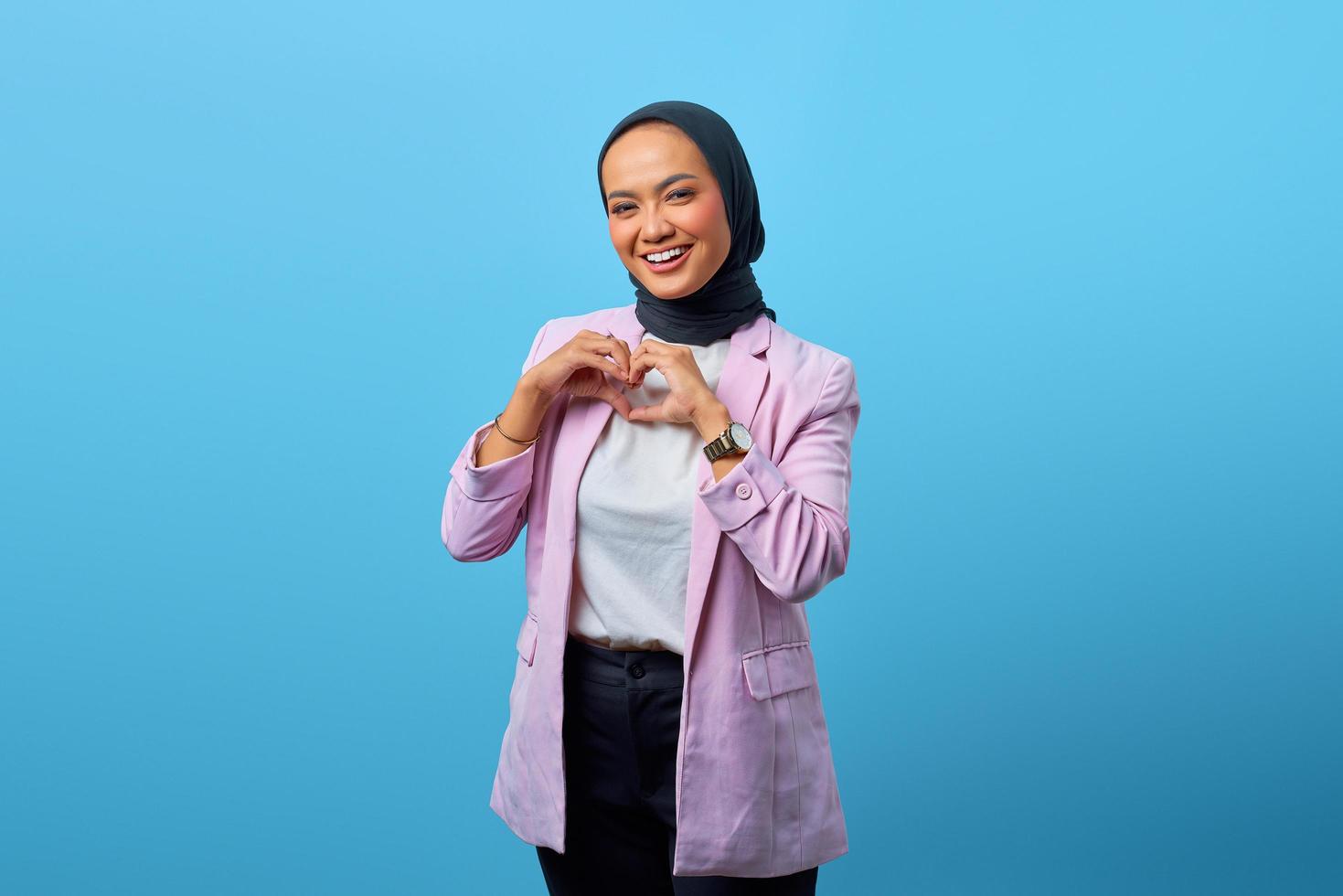 schöne asiatische Frau, die Formherzgeste über blauem Hintergrund zeigt foto