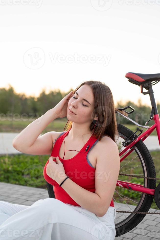 Teenager, der bei Sonnenuntergang an ihrem Fahrrad sitzt und Musik im Park hört foto
