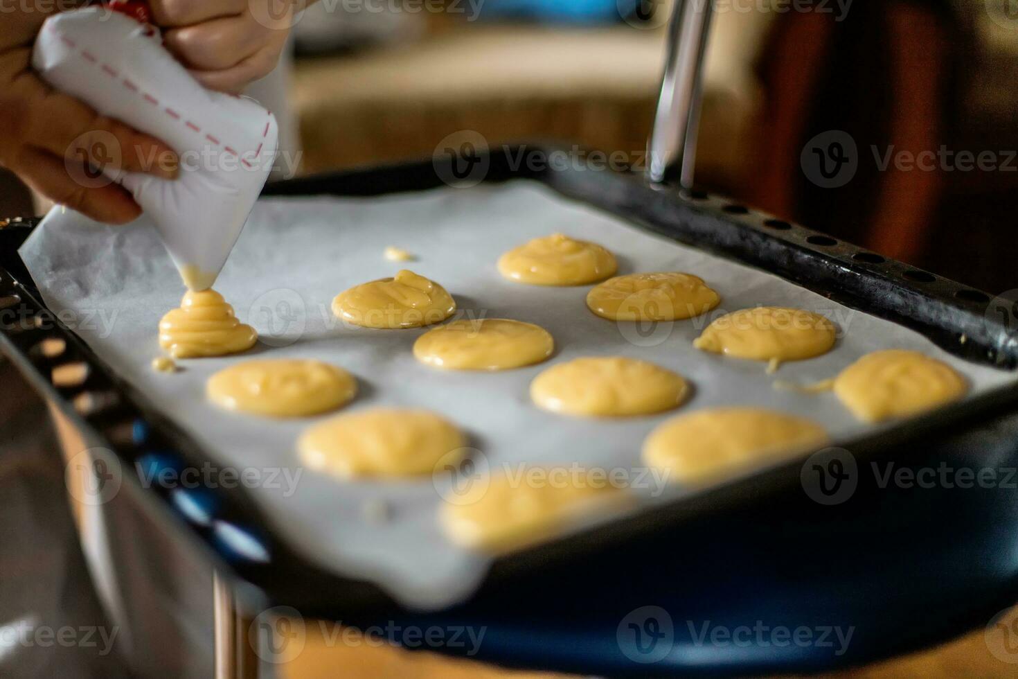 Hand quetschen aus von Süßwaren Tasche Teig zum Pudding Kuchen. Pudding Teig köstlich Sahne Puff Kuchen auf Backen Tablett. Pudding Kuchen Profiteroles Vor Platzierung im Ofen foto