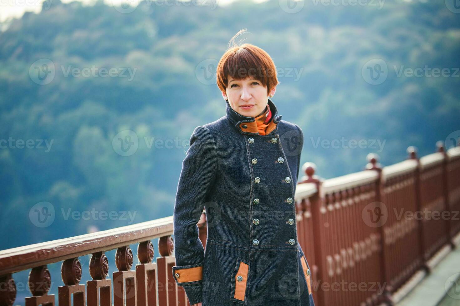 jung Frau Stehen auf ein Fußgänger Brücke im Kiew. das Frau mit kurz Haar gelehnt auf das Brücke Geländer. Frau auf das Hintergrund von Kiew Landschaft. foto