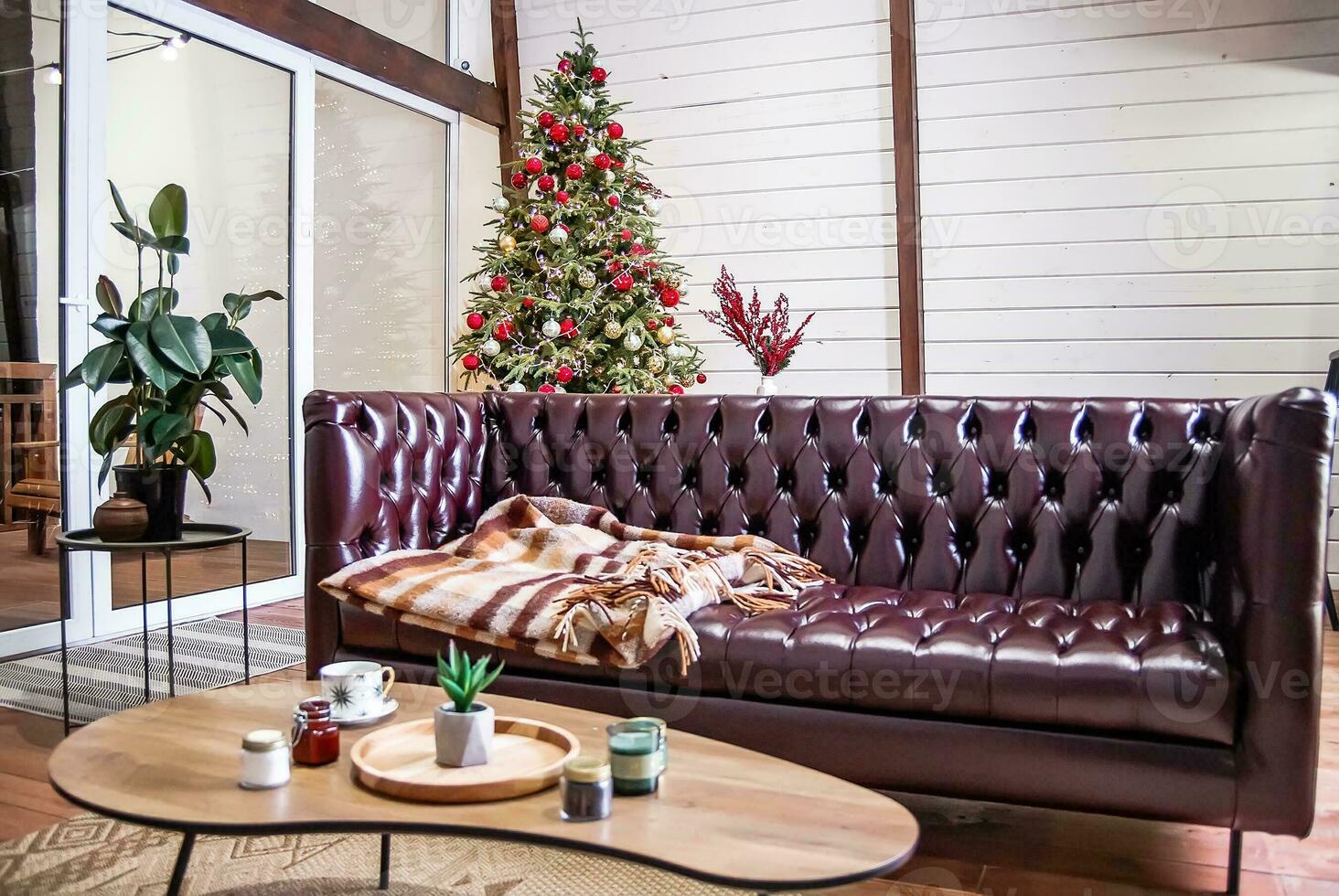 Zimmer im Hugo mit Weihnachten Baum. Leder braun Sofa mit Plaid in der Nähe von das serviert Urlaub Tisch. foto