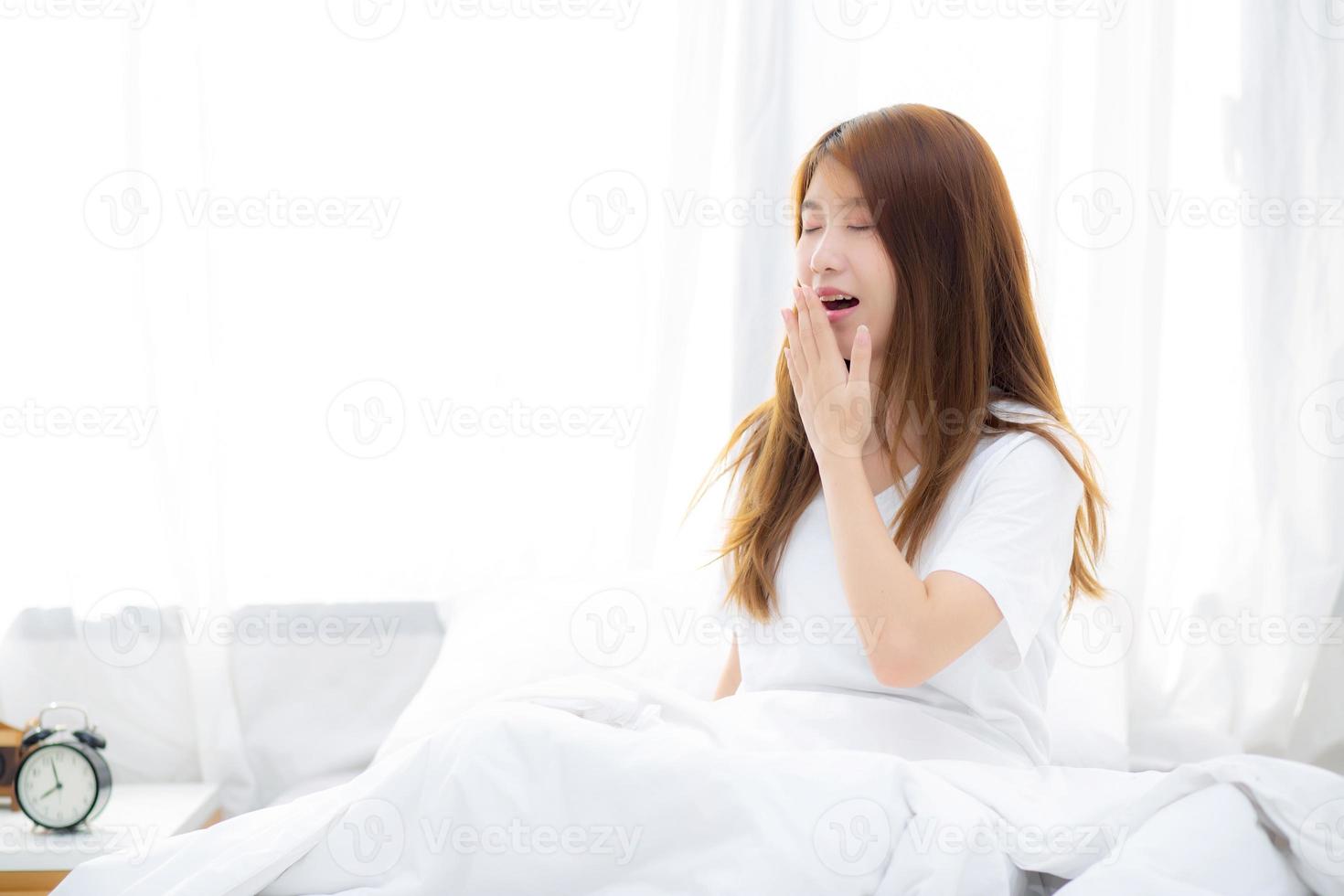 schön des Porträts junge asiatische Frau gähnt mit Schlaf auf dem Bett im Schlafzimmer, Mädchen wacht nach Ruhe und Freizeit mit Wellness, Lifestyle-Konzept auf. foto