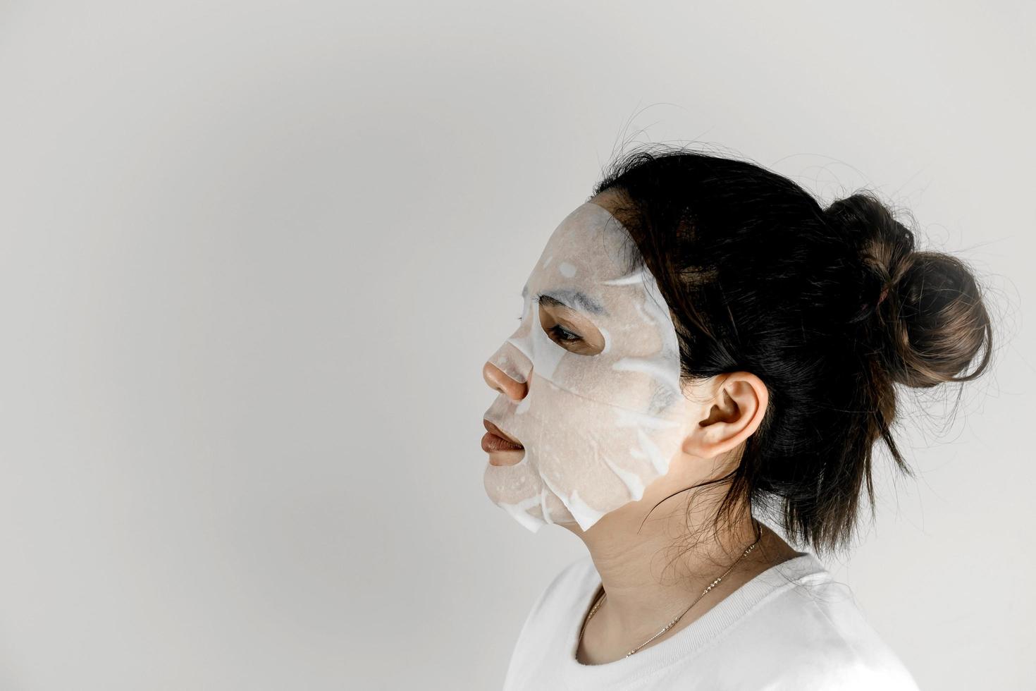 asiatische frau im weißen t-shirt und bedeckt ihr gesicht mit einer blattmaske. foto