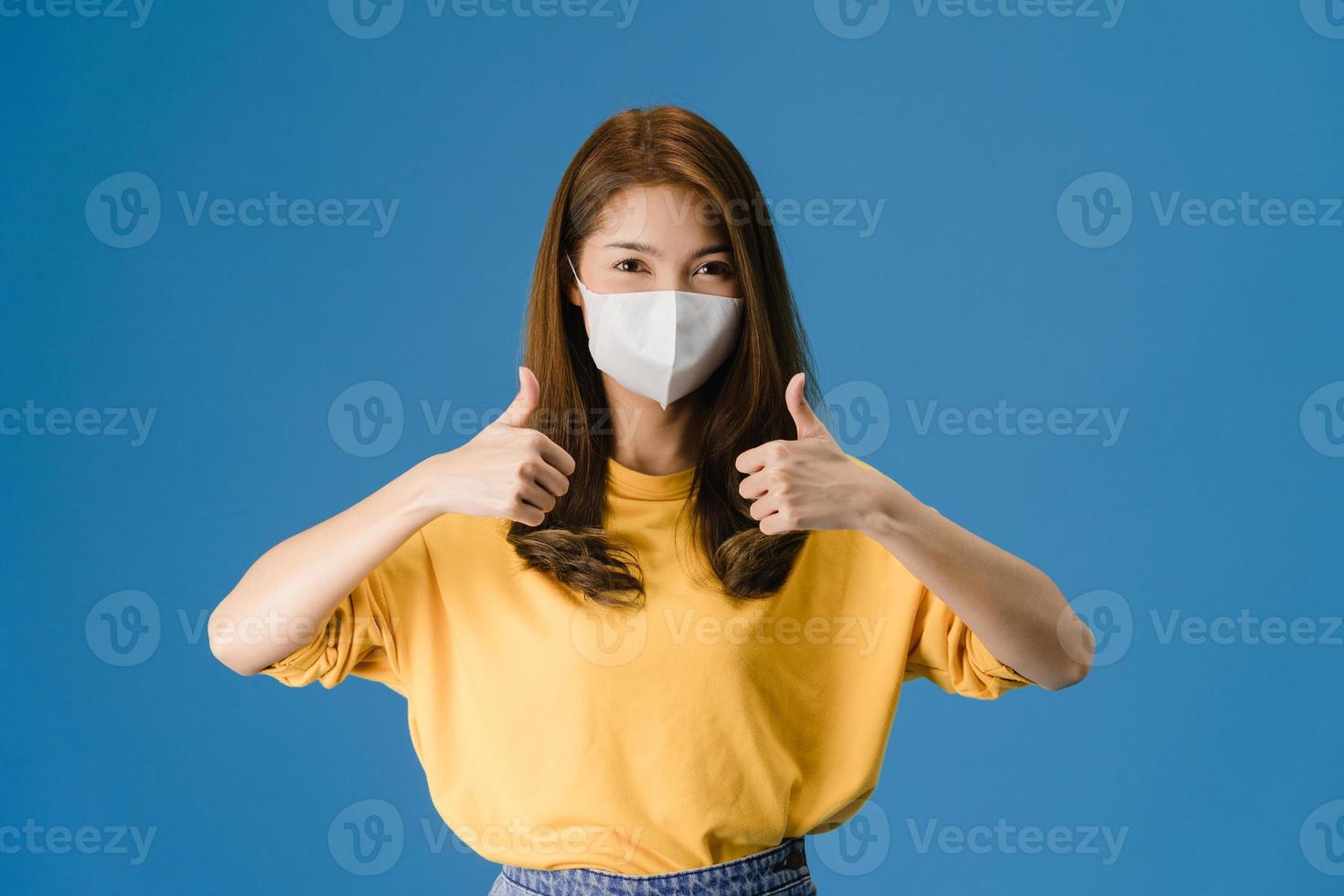junge asiatische Mädchen tragen Gesichtsmaske mit Daumen nach oben auf blauem Hintergrund. foto