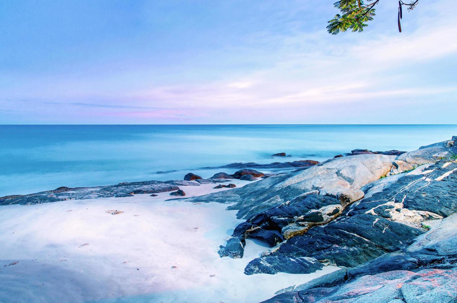 der Blick auf den Sandstrand und die Meereswelle mit Felsen und Riff am Morgen foto