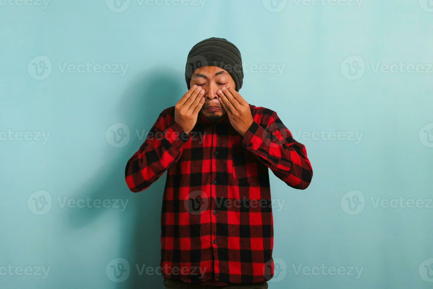 jung asiatisch Mann Reiben seine geschwollen Augen fällig zu Staub Allergie und Juckreiz isoliert auf Blau Hintergrund foto