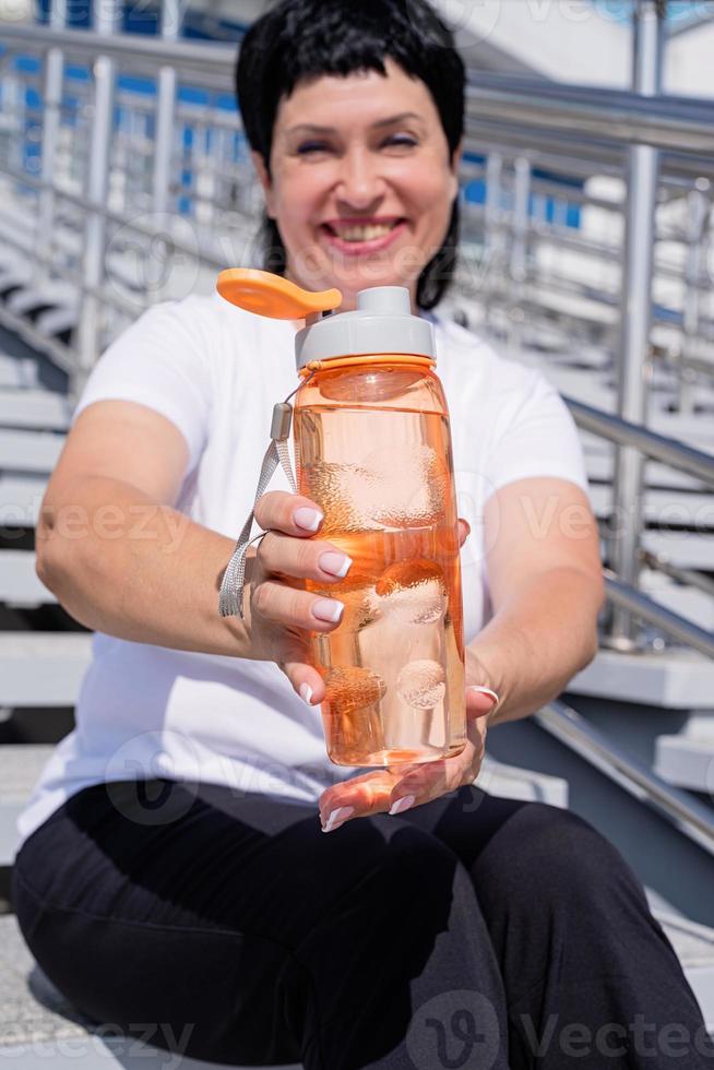 ältere Frau trinkt Wasser nach dem Training im Freien auf städtischem Hintergrund foto