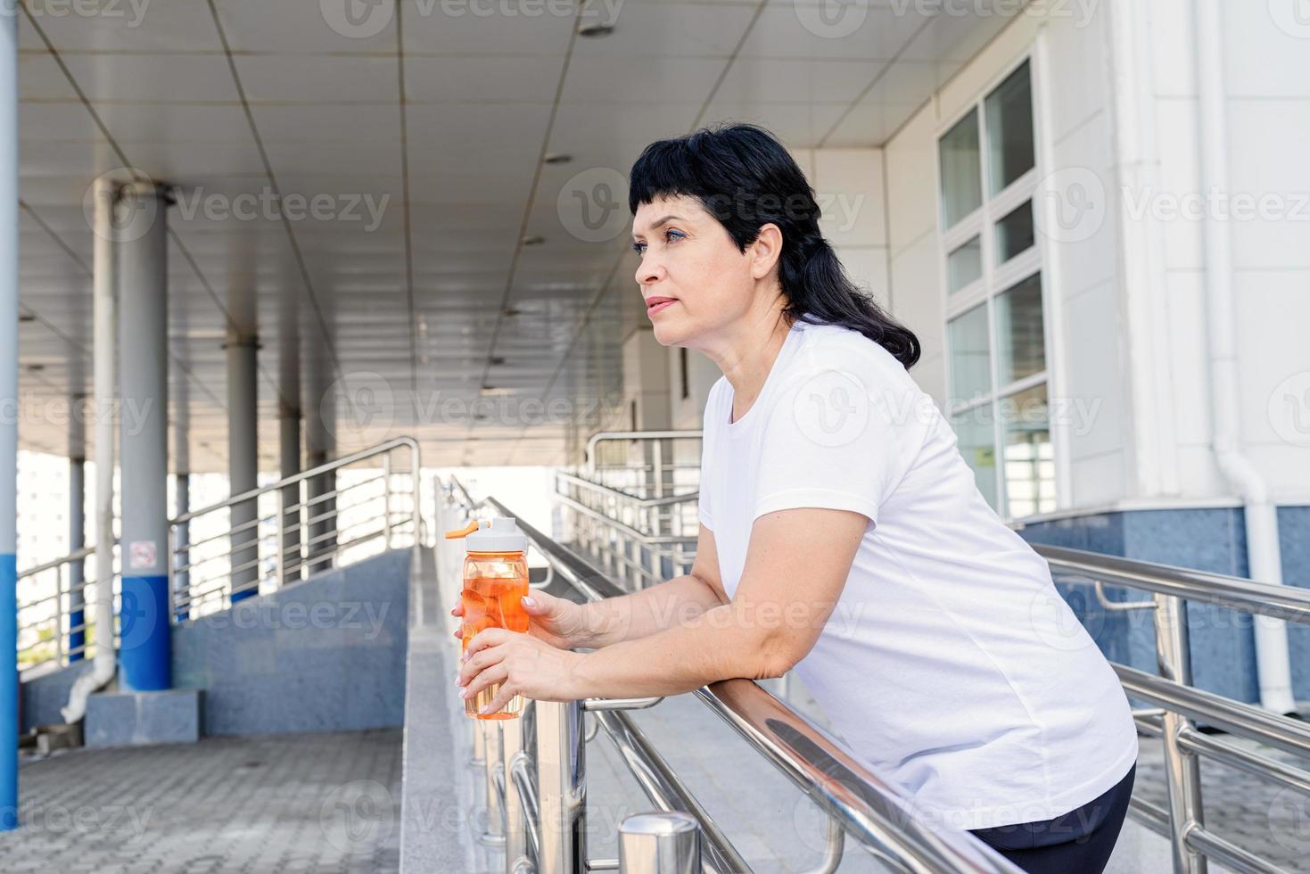 ältere Frau trinkt Wasser nach dem Training im Freien auf städtischem Hintergrund foto
