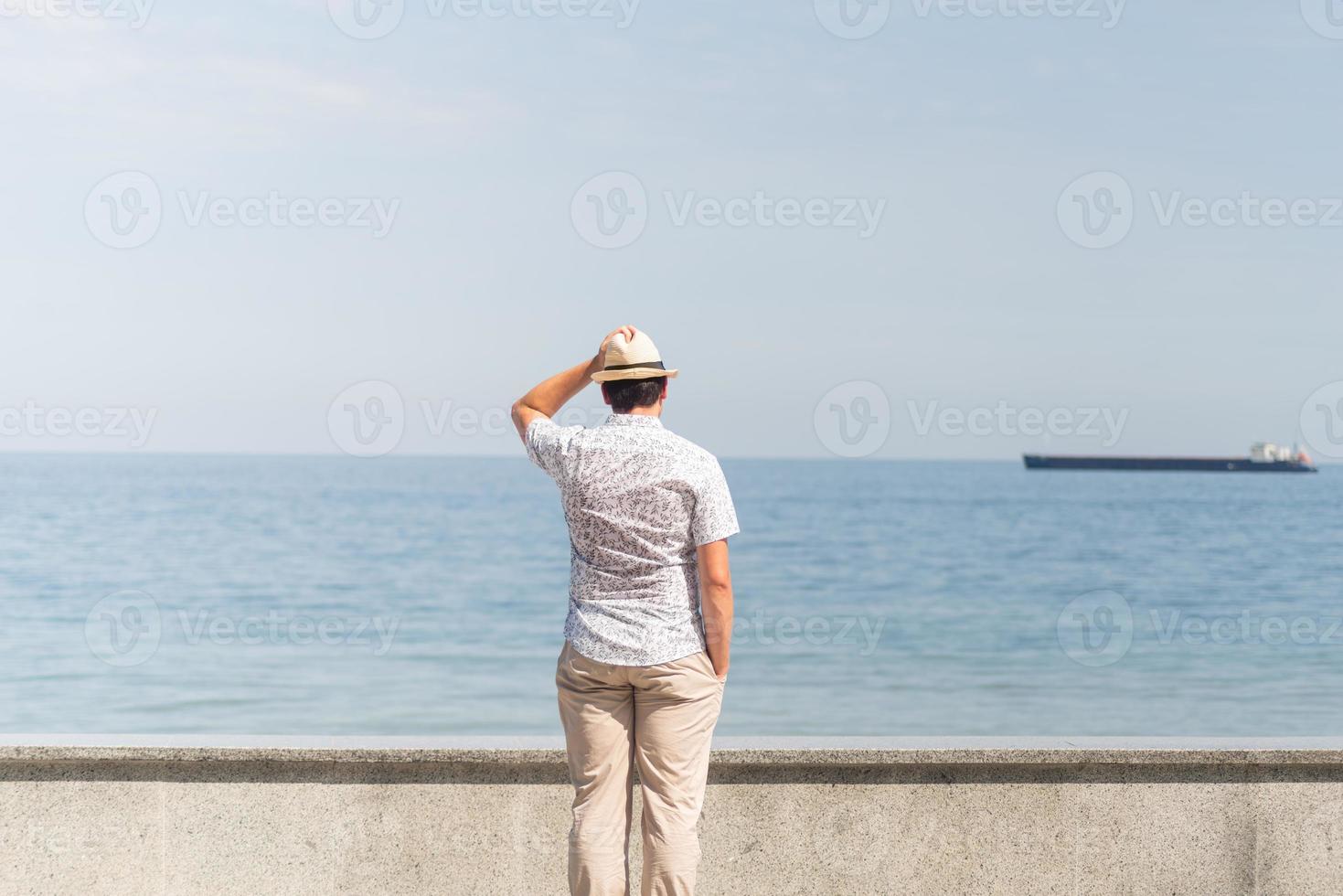 junger Mann in Sommerkleidung steht auf einem Pier, Meer im Hintergrund foto