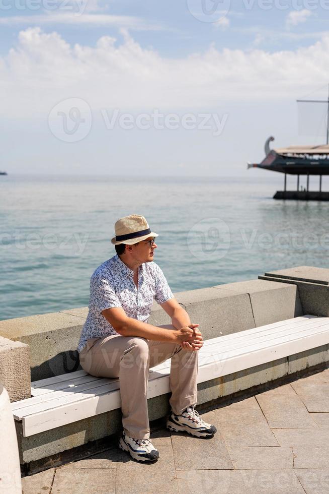 junger Mann sitzt auf der Bank am Meer foto