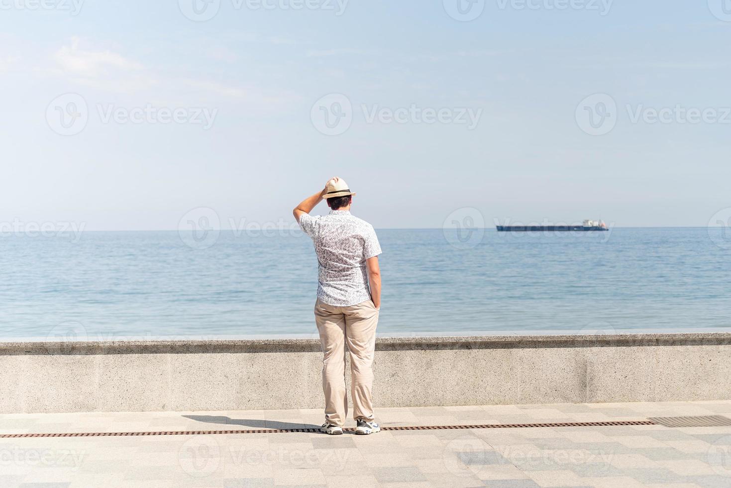 junger Mann in Sommerkleidung steht auf einem Pier, Meer im Hintergrund foto