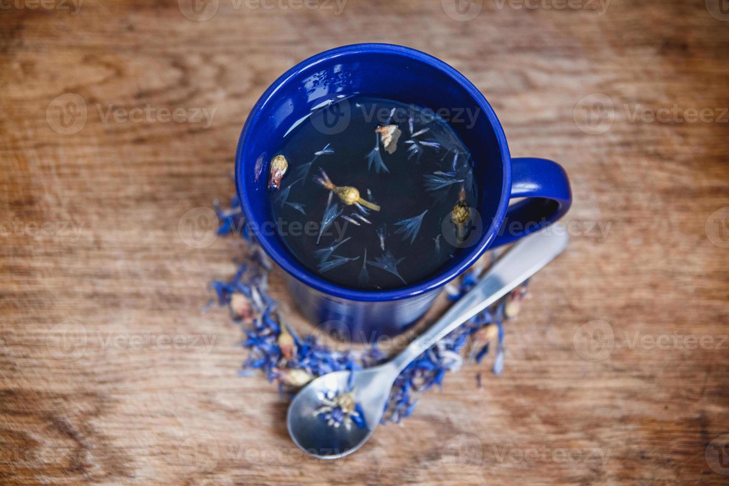 blaue Tasse und Löffel mit geblümtem Schwarztee auf Holzuntergrund foto