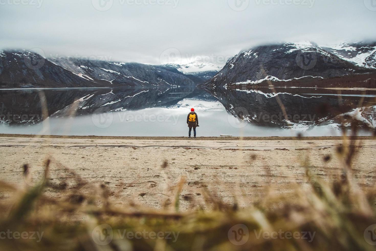 Mann, der auf dem Hintergrund von Bergen und See steht, macht ein Foto