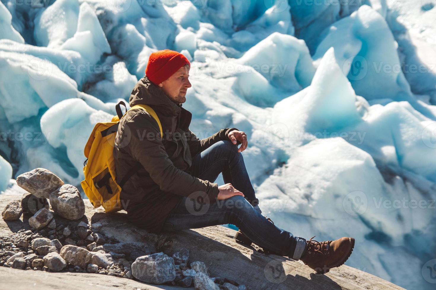 Reisender Mann sitzt auf einem Felsen auf dem Hintergrund eines Gletschers und Schnee foto