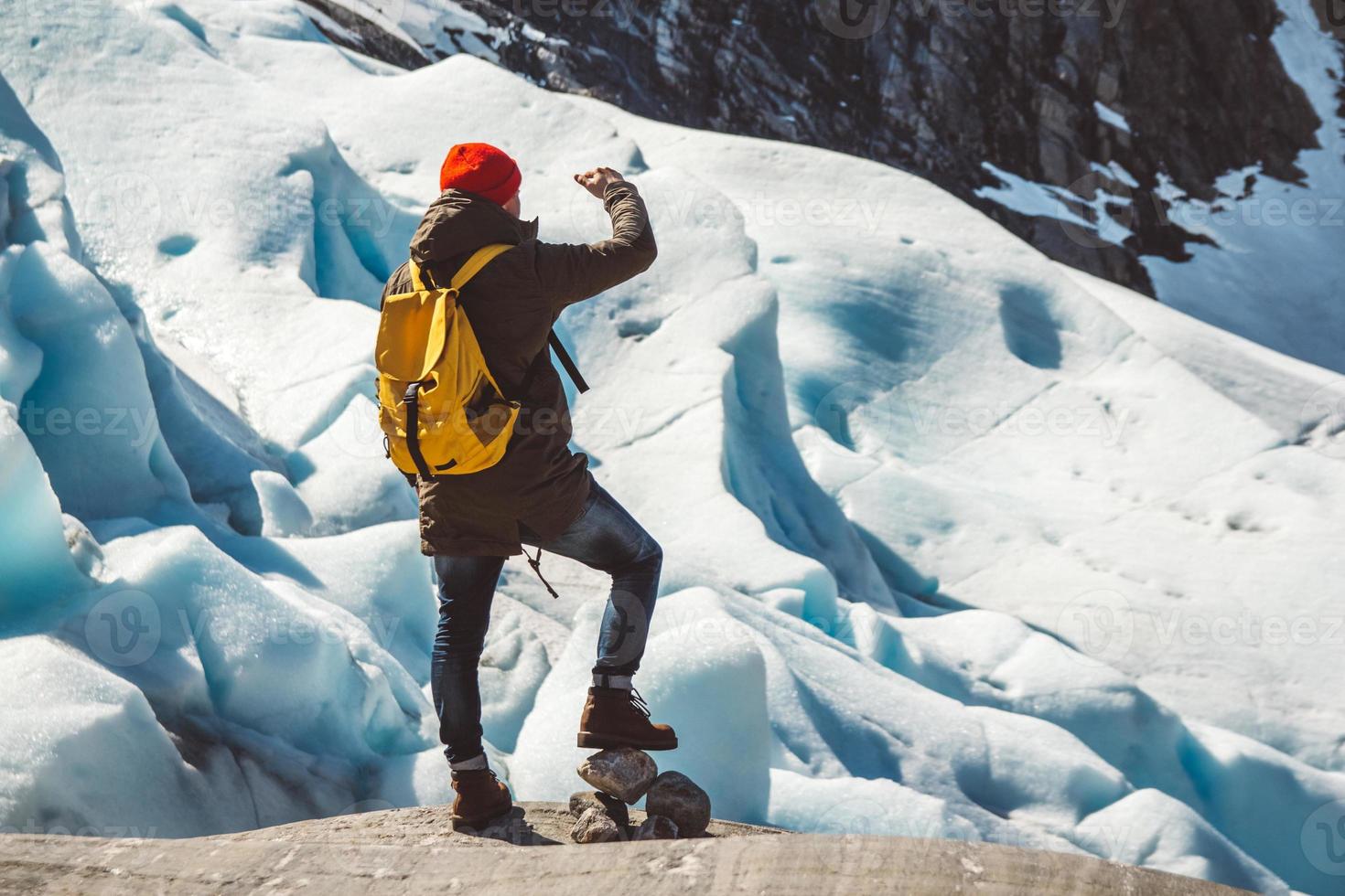 Reisender Mann, der auf einem Felsen auf dem Hintergrund eines Gletschers steht foto