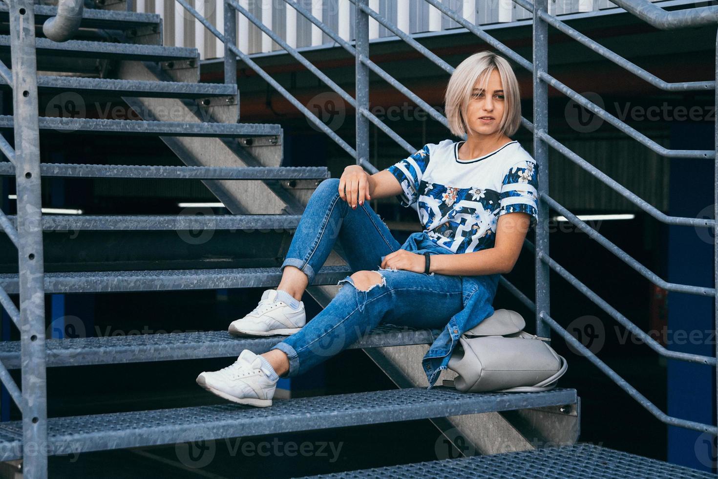 Frau mit kurzen weißen Haaren im urbanen Stil sitzt auf der Metalltreppe foto