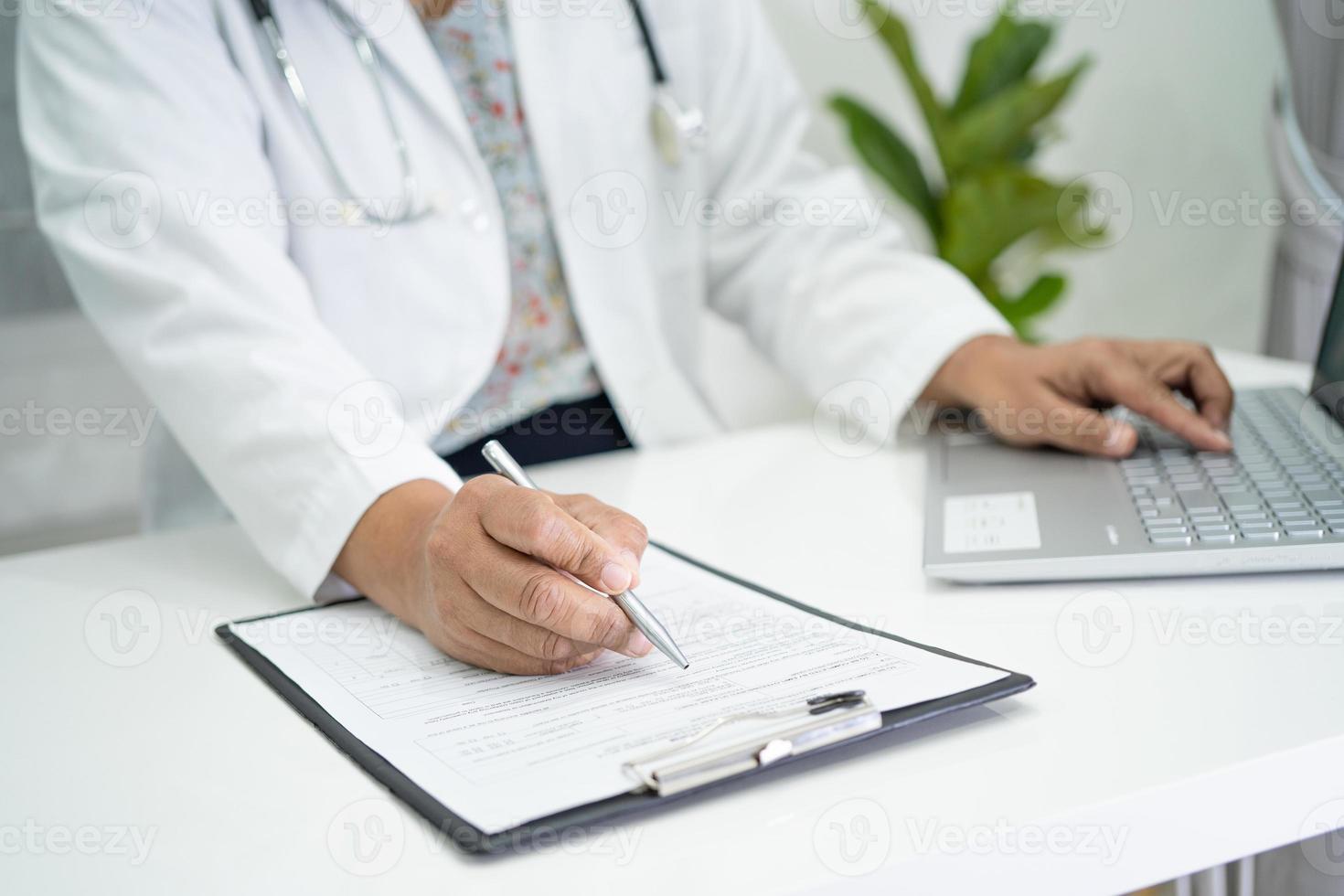 Arzt schreiben Gesundheitsnotiz in Zwischenablage mit Laptop im Krankenhaus. foto