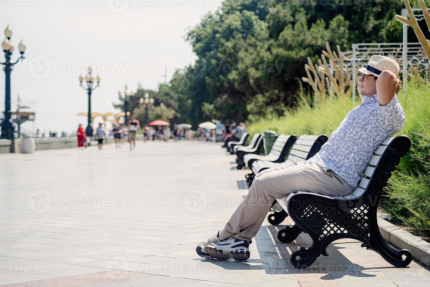 Mann in Sommerkleidung sitzt auf der Bank am Ufer des Meeres foto