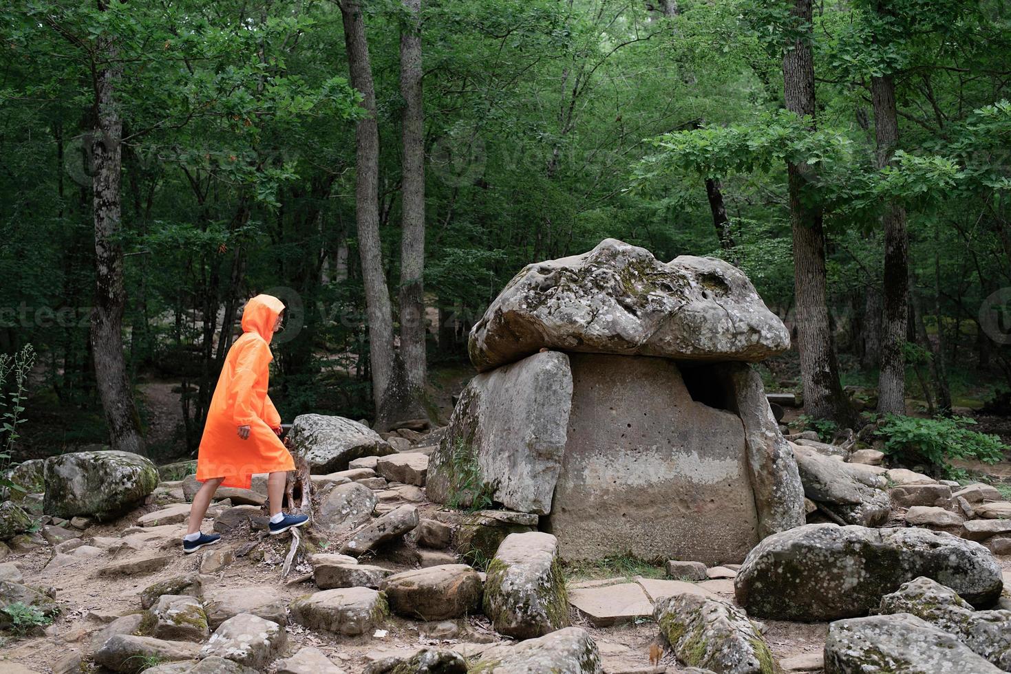 glückliche Frau im orangefarbenen Regenmantel, die im Wald spazieren geht foto