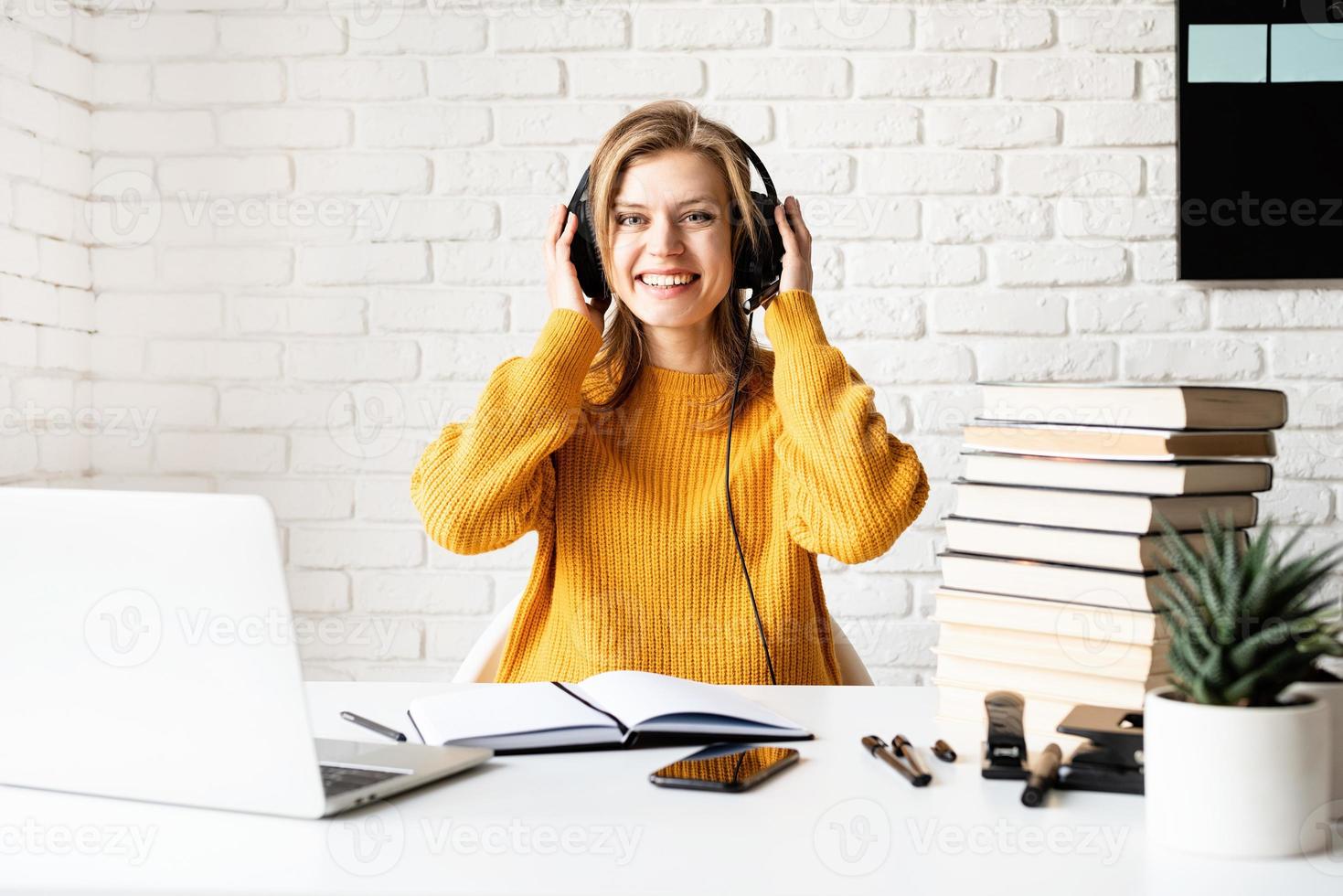 junge lächelnde Frau in schwarzen Kopfhörern, die online mit Laptop studiert? foto