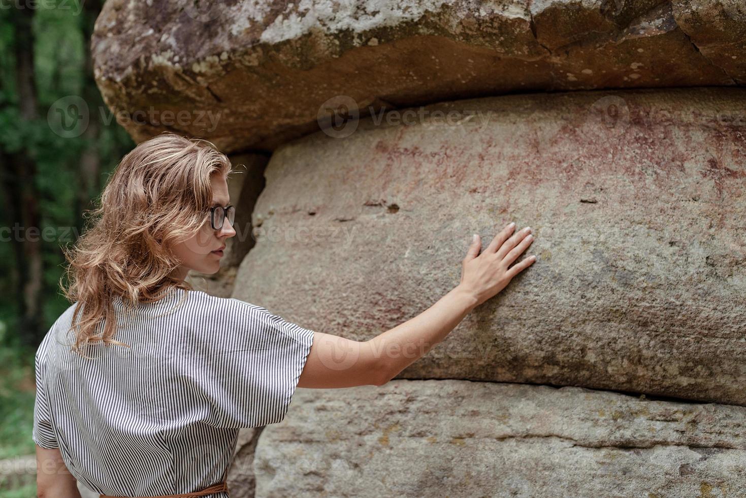 junge Frau, die in der Nähe eines großen Dolmensteins im Wald spazieren geht foto