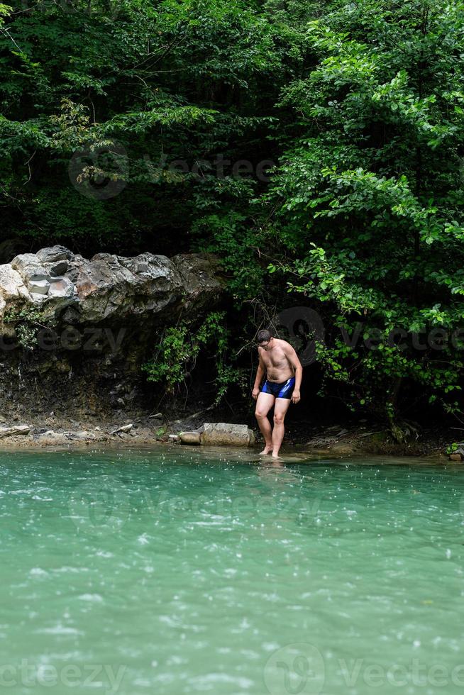 Mann schwimmt im Bergfluss mit Wasserfall foto