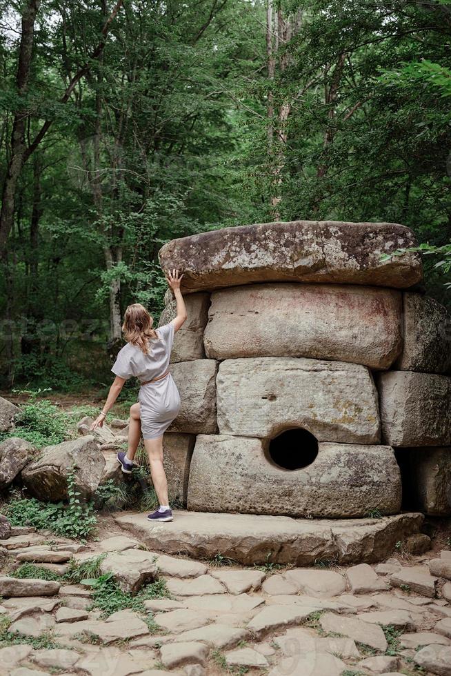 junge Frau, die in der Nähe eines großen Dolmensteins im Wald spazieren geht foto