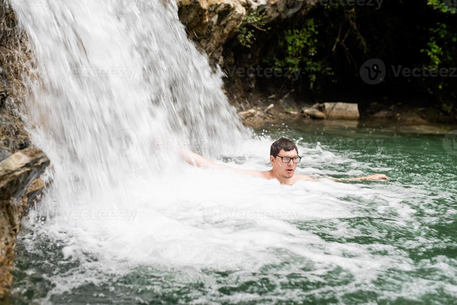 Mann schwimmt im Bergfluss mit Wasserfall foto