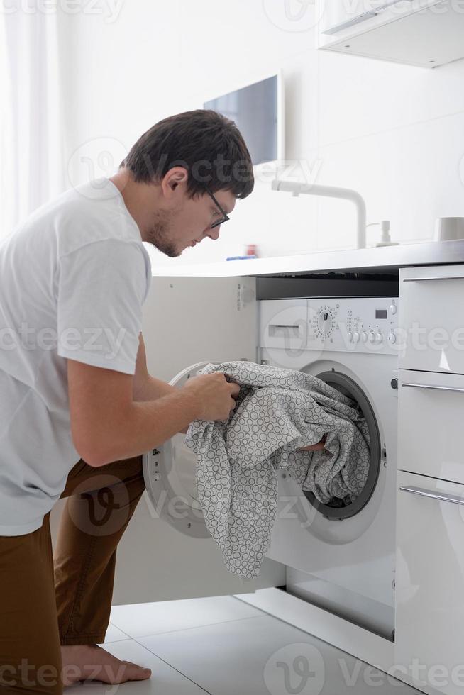 junger Mann steckt Kleidung in die Waschmaschine foto
