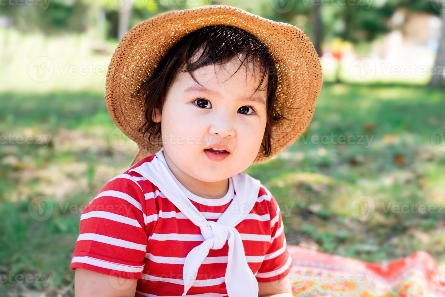 süßes kleines Baby in einem roten Kleid und Hut auf einem Picknick im Park foto