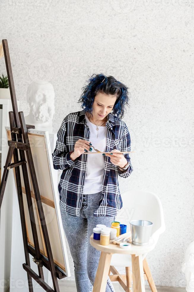 Kreative Frau mit blau gefärbten Haaren malt in ihrem Atelier foto