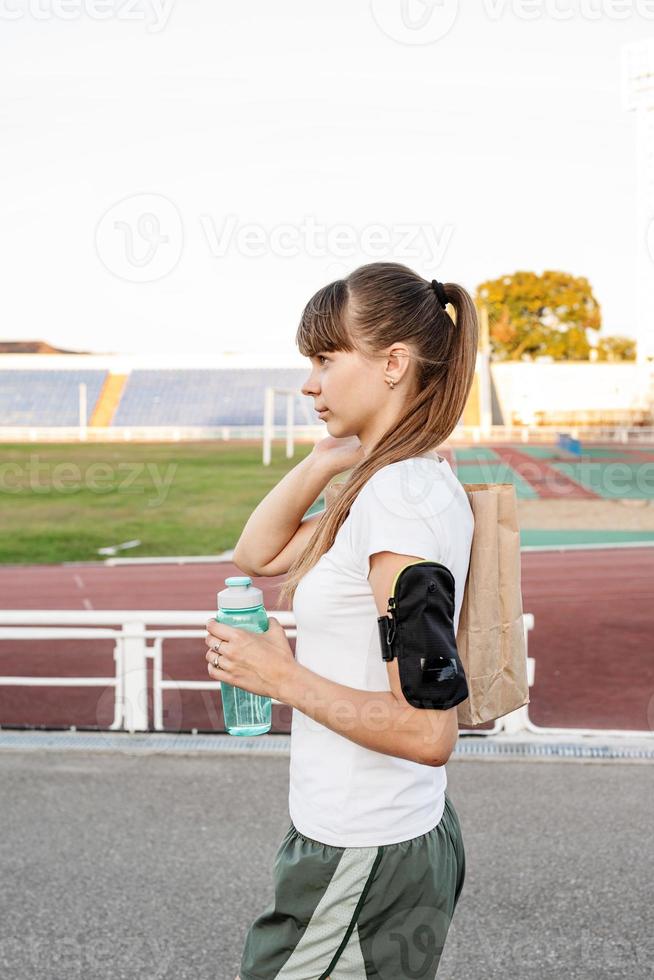 Teenager-Mädchen, das nach dem Training mit der Papiertüte im Stadion spazieren geht foto