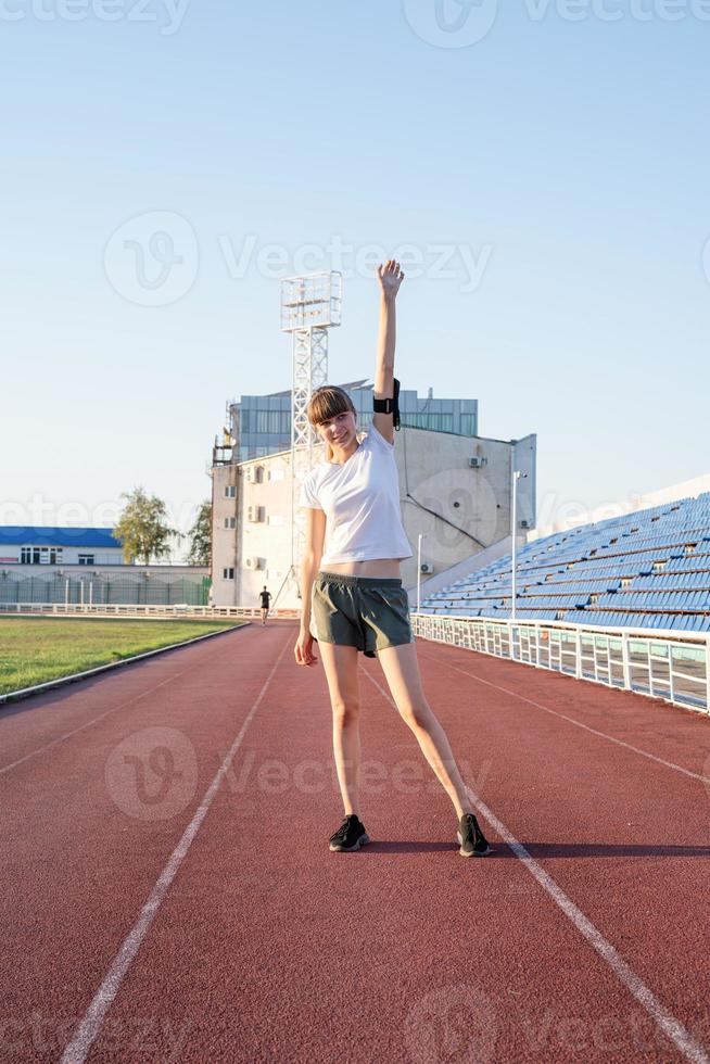 junges Sportmädchen, das auf der Strecke steht und ihre Arme hebt foto