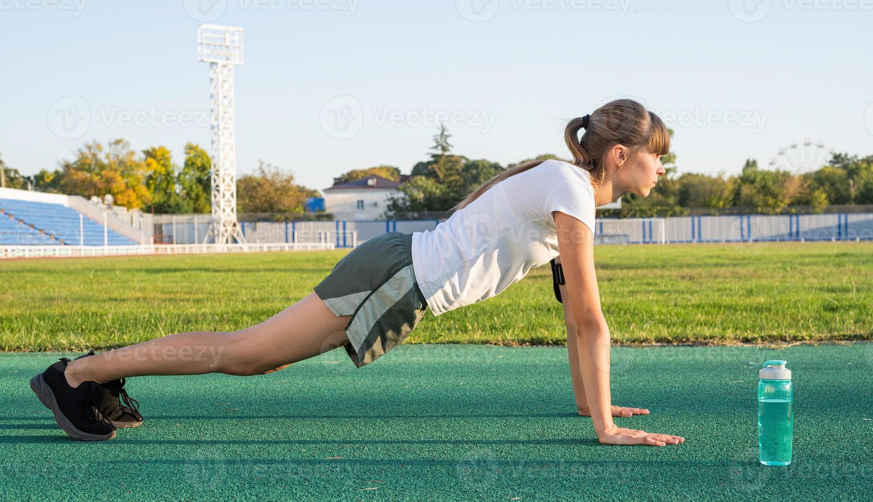 Teenager-Mädchen-Training steht in einer Plankenposition im Stadion foto