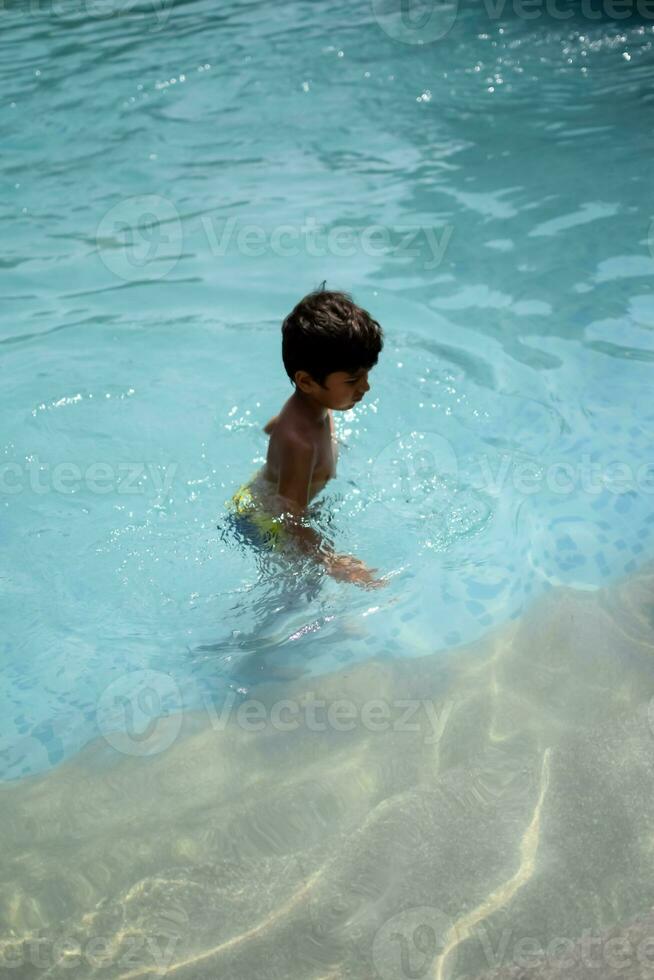 glücklich indisch Junge Schwimmen im ein Schwimmbad, Kind tragen Schwimmen Kostüm entlang mit Luft Tube während heiß Sommer- Urlaube, Kinder Junge im groß Schwimmen Schwimmbad. foto