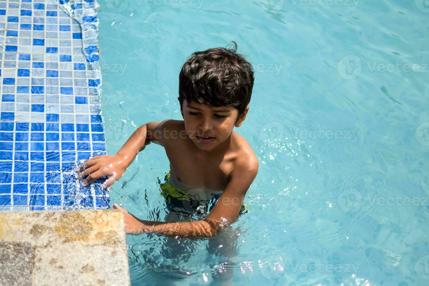 glücklich indisch Junge Schwimmen im ein Schwimmbad, Kind tragen Schwimmen Kostüm entlang mit Luft Tube während heiß Sommer- Urlaube, Kinder Junge im groß Schwimmen Schwimmbad. foto