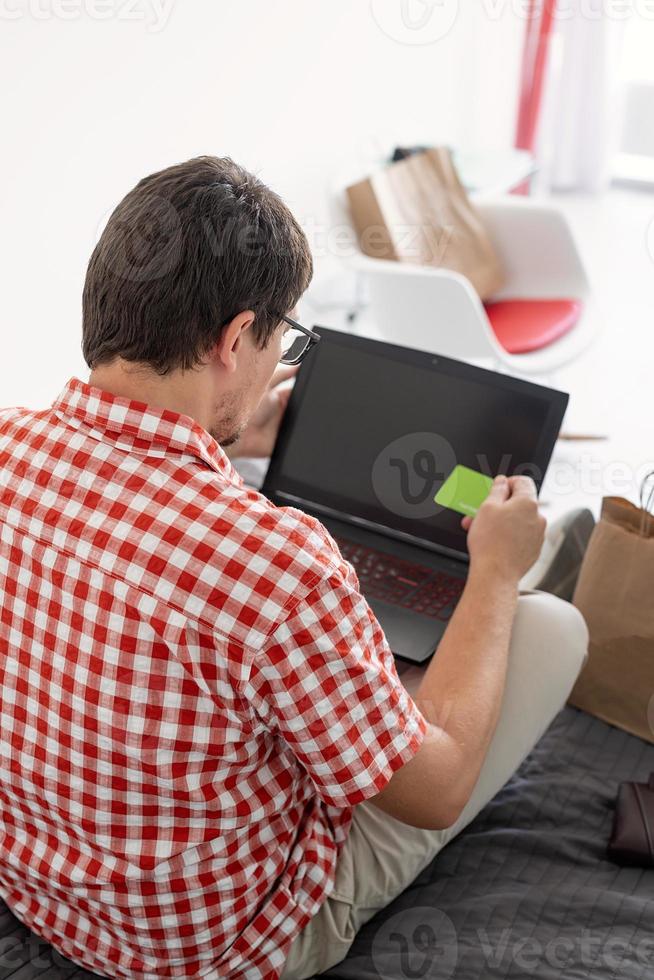 Rückansicht des Mannes beim Einkaufen im Internet mit Laptop suchen foto