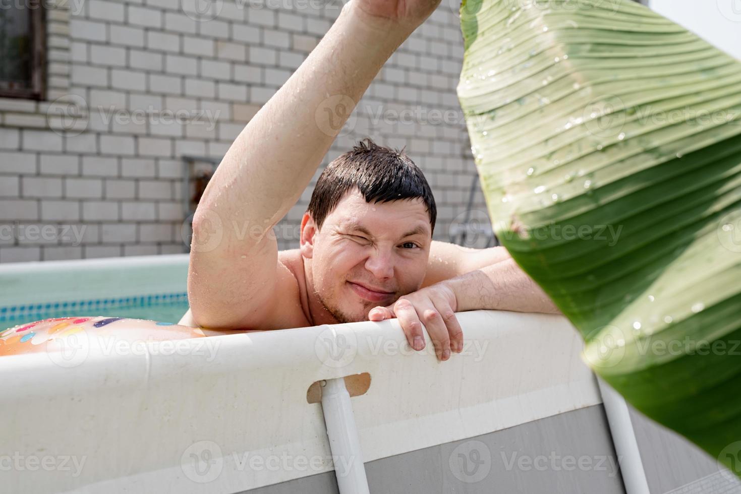 junger Mann, der im Schwimmbad schwimmt und ein Palmblatt hält foto