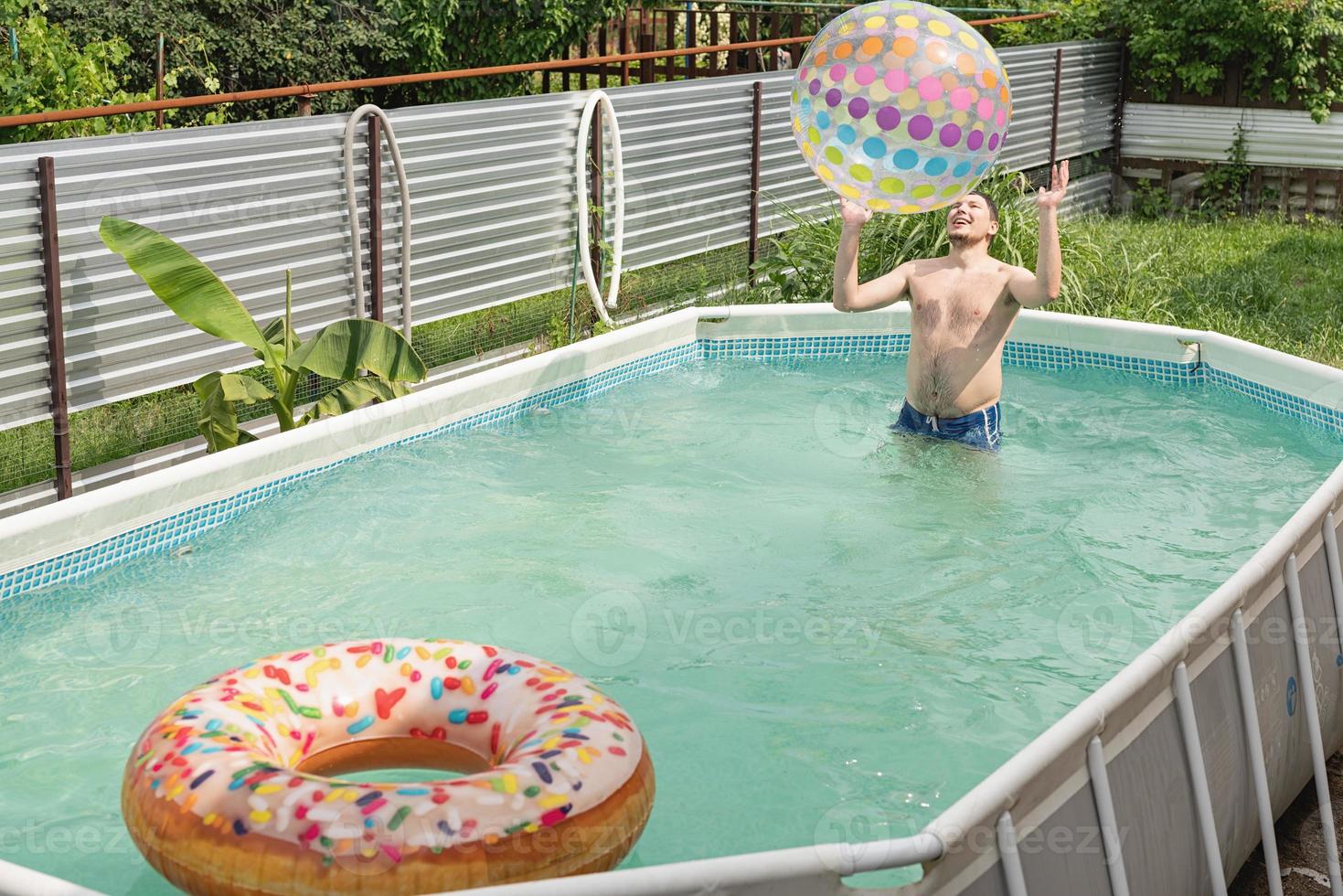 Mann hat Spaß im Schwimmbad und spielt mit aufblasbarem Ball foto